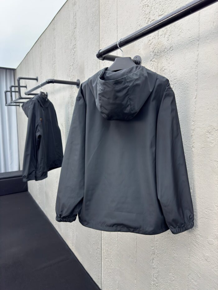 Giaccone grigio minimalista su appendiabiti nero in ambiente moderno e luminoso.