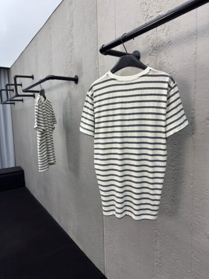 Camicie a strisce minimaliste su supporti neri in un ambiente moderno con parete in cemento levigato.