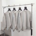 Vetrina moderna con maglioni grigi minimalisti su appendini neri, stile semplice e contemporaneo.