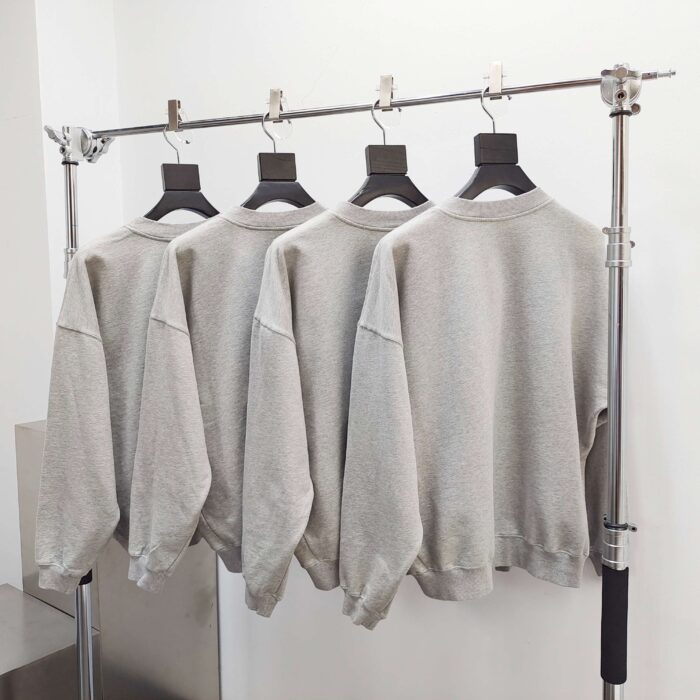 Vetrina moderna con maglioni grigi minimalisti su appendini neri, stile semplice e contemporaneo.