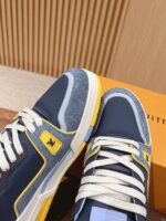 Sneakers moderne in navy, giallo e grigio con logo giallo e packaging arancione elegante.