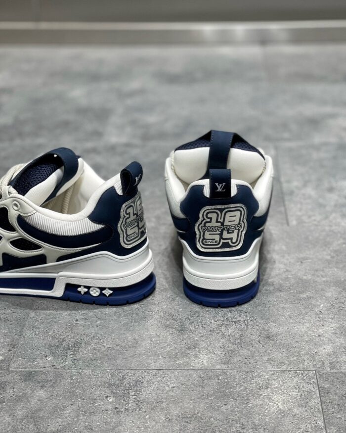 Sneaker navy e bianco con logo stilizzato, design moderno e suola resistente, stile casual e sportivo.