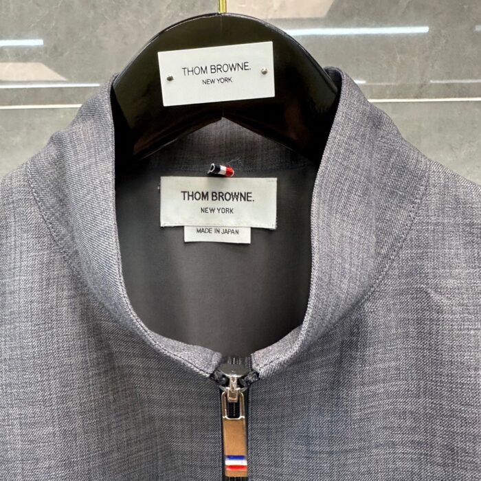 Giacca Thom Browne con colletto alto, zip elegante e dettagli iconici in stile moderno e sofisticato.