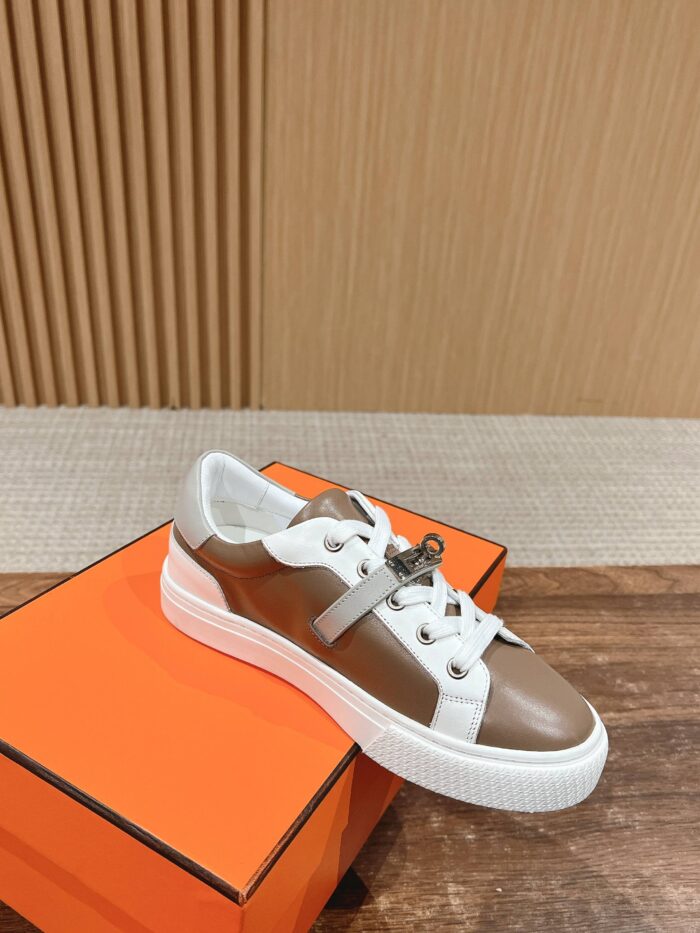 Sneaker in pelle marrone e bianco con dettagli eleganti su superficie di legno.