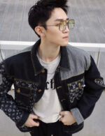 Giovane uomo fashion con giacca patchwork, occhiali trendy e stile urbano moderno.