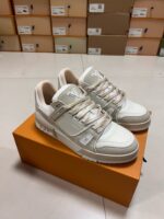 Sneakers bianche moderne con dettagli beige su scatola arancione, ambiente di vendita ordinato.