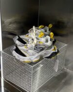 Sneakers bianche e gialle in esposizione moderna con suola chunky, su base diamantata e display trasparente.