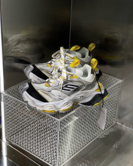 Sneakers bianche e gialle in esposizione moderna con suola chunky, su base diamantata e display trasparente.