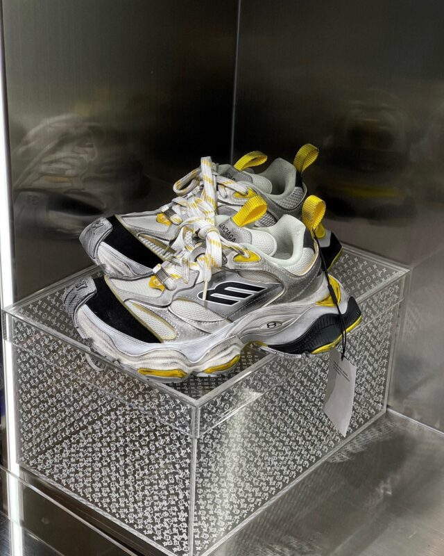 Sneakers bianche e gialle in esposizione moderna con suola chunky, su base diamantata e display trasparente.