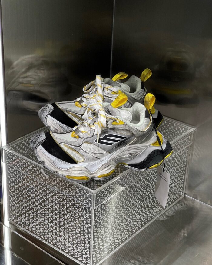 Sneakers bianche e gialle in esposizione moderna con suola chunky, su base diamantata e display trasparente.
