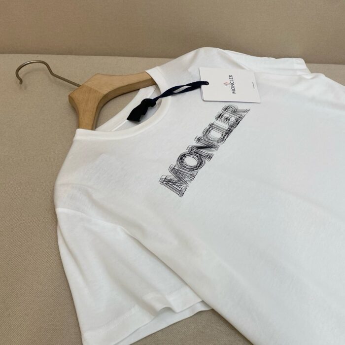 Maglietta bianca Moncler su appendiabiti in legno, stile minimalista e design elegante.