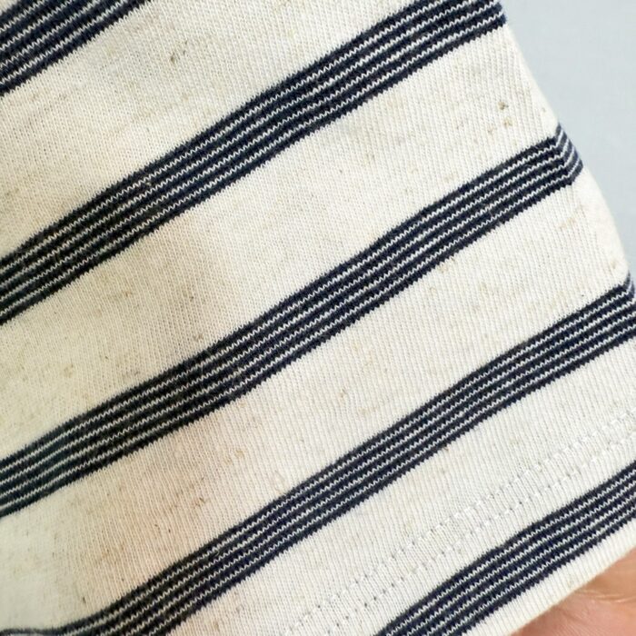 Dettaglio di polsino a righe navy e beige in tessuto naturale e morbido.
