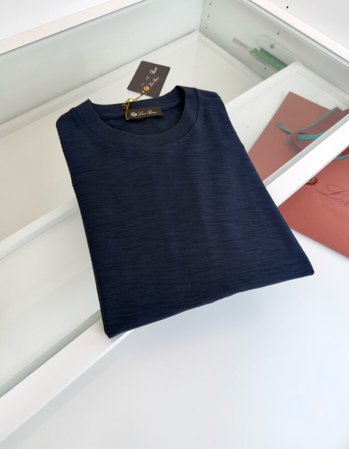 Maglietta navy blue piegata su superficie bianca, stile minimalista ed elegante per casual wear.