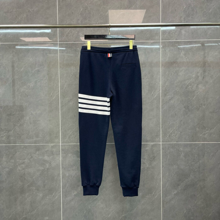 Pantaloni jogger navy blu con bande bianche, stile sportivo e comfort, su sfondo grigio.