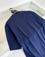Maglietta Navy blu semplice e versatile, vista posteriore su manico nero, riflesso su superficie vetrata.