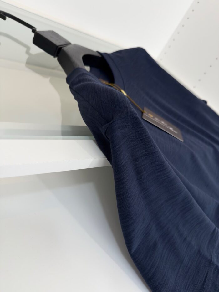 Maglietta blu navy elegante su appendiabiti moderno, tessuto morbido e finitura raffinata.