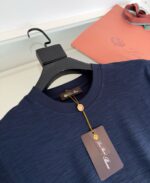 Maglietta navy blue con dettaglio elegante, etichetta e accessori di lusso in presentazione raffinata.