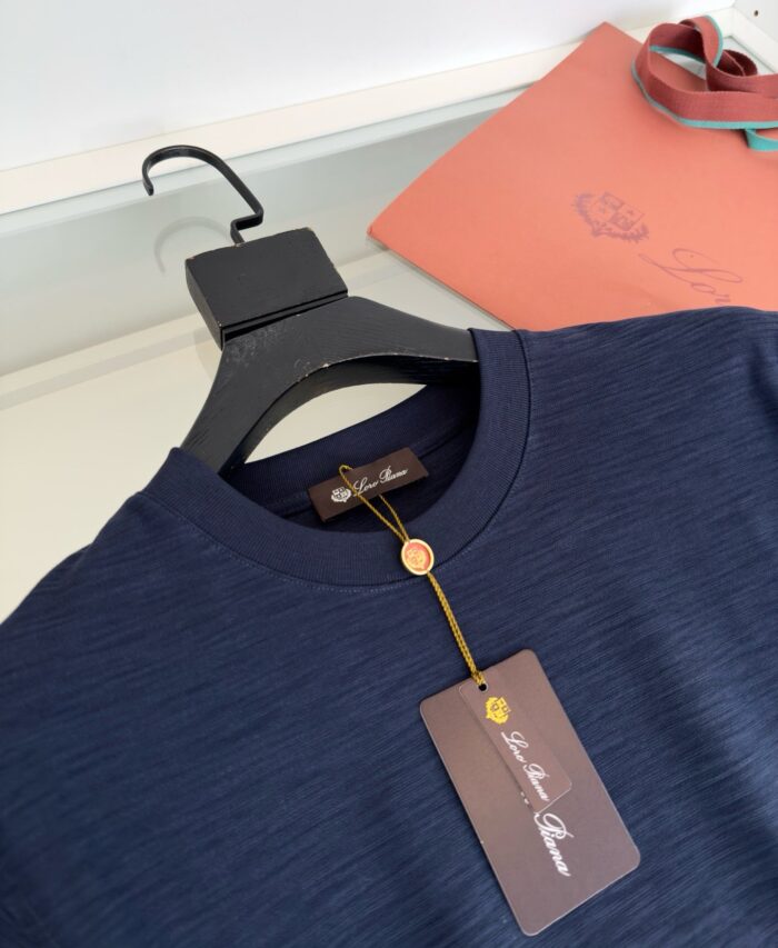 Maglietta navy blue con dettaglio elegante, etichetta e accessori di lusso in presentazione raffinata.