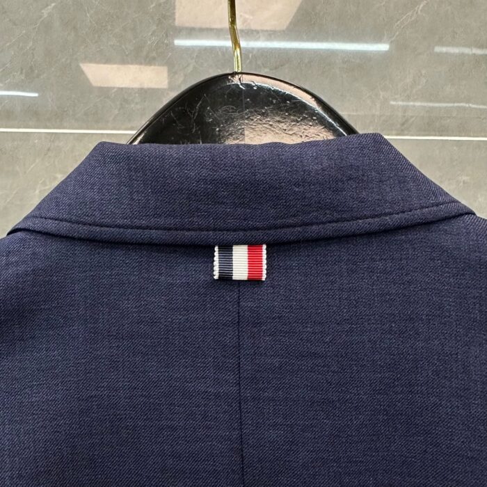 Dettaglio del colletto navy con etichetta a strisce rosso, bianco e blu, stile elegante e moderno.