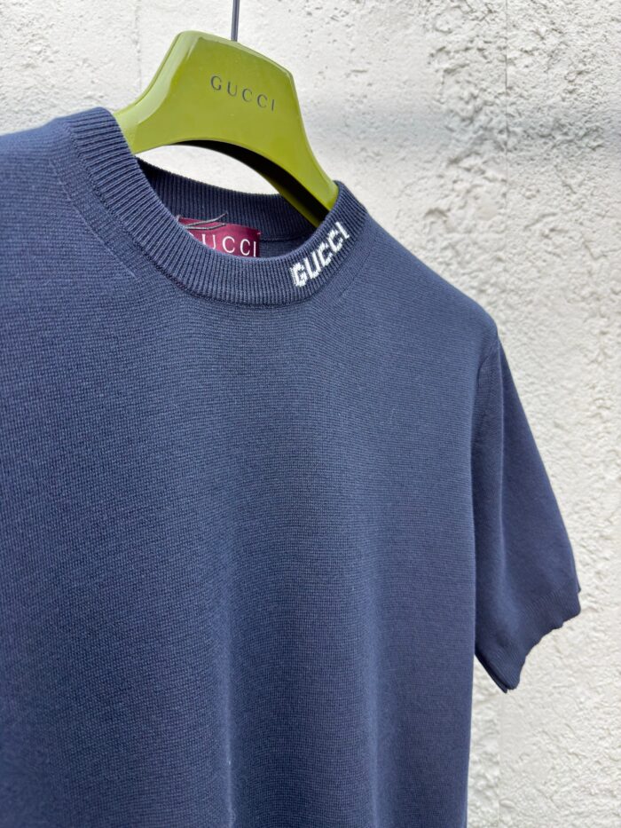 T-shirt Gucci navy con colletto bianco, su gruccia verde brillante, stile elegante e casual.