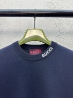 Felpa Gucci blu navy con ricamo bianco, impostata su gruccia verde, in sfondo bianco testurizzato.