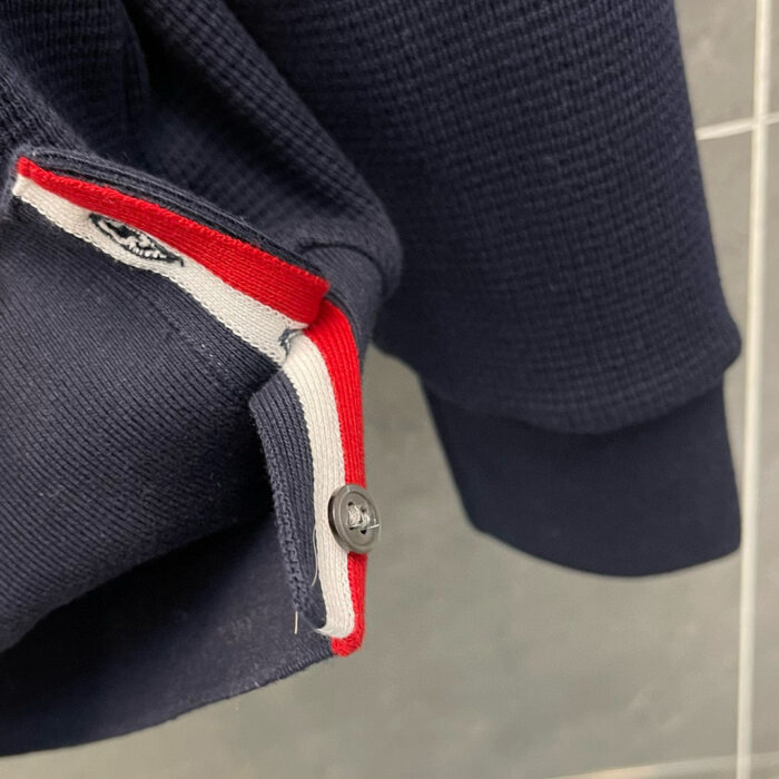 Maglietta navy con polsini sportivi a banda colorata e dettaglio con bottone, stile casual ed elegante.