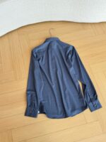 Camicia blu maniche lunghe in tessuto elegante su pavimento di legno, stile sofisticato e versatile.