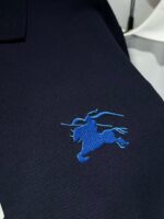Maglietta polo navy con ricamo cavalleresco blu, stile elegante e casual con camicia bianca stratificata.