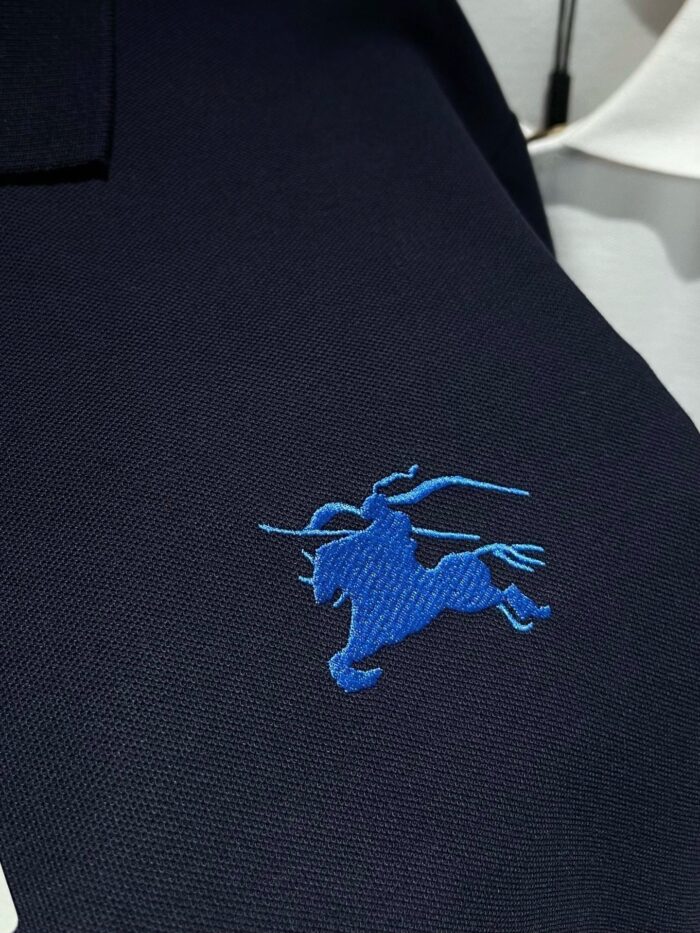 Maglietta polo navy con ricamo cavalleresco blu, stile elegante e casual con camicia bianca stratificata.