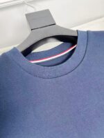 Maglione navy con dettaglio a strisce, girocollo classico e stile sportivo, su appendiabiti nero raffinato.