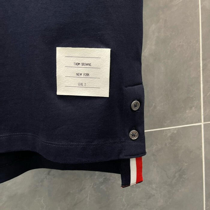 T-shirt navy casual con etichetta bianca, bottoni metallici e dettaglio a righe rosse e bianche.