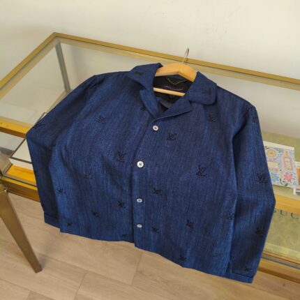 Camicia cropped in denim blu con ricami neri e bottoni bianchi su tavolo di vetro.