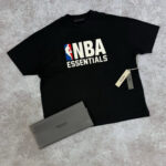 Maglietta NBA Essentials nera con logo e portafoglio grigio minimalista stile urbano.