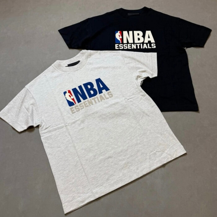 Magliette NBA Essentials grigia e nera con logo e testo contrastati, stile sportivo e casual.
