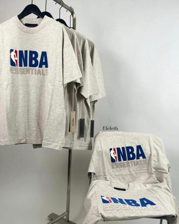Maglietta NBA Essentials grigia, logo prominente, stile casual, perfetta per basket e streetwear.