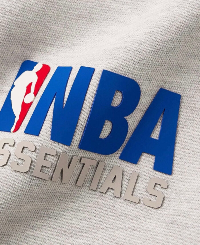 Maglietta grigia NBA Essentials con logo blu, stile casual e sportivo, tessuto confortevole.