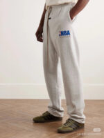 Pantaloni sportivi grigi con logo NBA e sneakers olive in look casual e trendy.