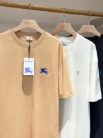 Set di T-shirt neutri beige, bianco e navy su appendiabiti in legno naturale.