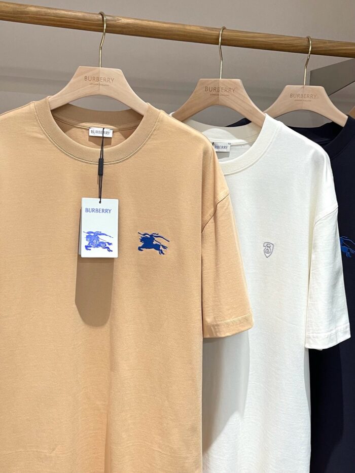 Set di T-shirt neutri beige, bianco e navy su appendiabiti in legno naturale.