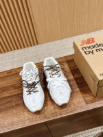Sneakers bianche New Balance con lacci marroni su superficie di legno chiaro.