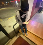 Ragazzo giovane in abbigliamento casual, snack notturno davanti a ristorante urbano illuminato.