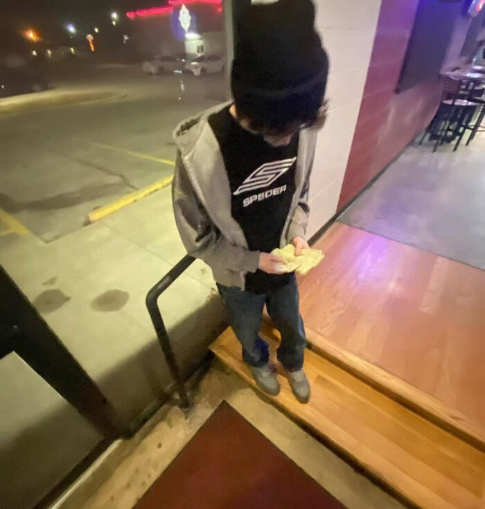 Ragazzo giovane in abbigliamento casual, snack notturno davanti a ristorante urbano illuminato.