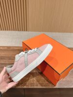 Sneaker rosa pastello con dettagli grigi, suola bianca e scatola arancione, stile casual e trendy.