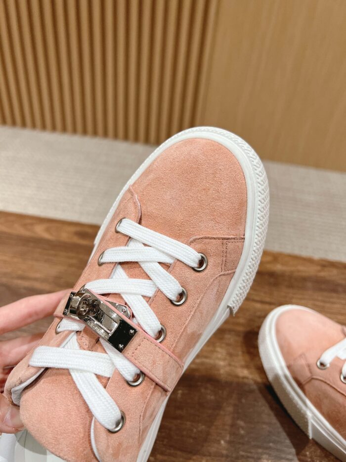 Sneaker rosa pastello in suede con lacci bianchi e dettaglio metallico, elegante e trendy.