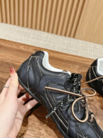 Scarpa sportiva nera con dettagli bianchi, design moderno, in mano su sfondo in legno caldo.