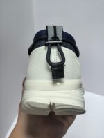 Scarpa sportiva moderna bianca con dettagli navy, tallone prominente e passante pratico.