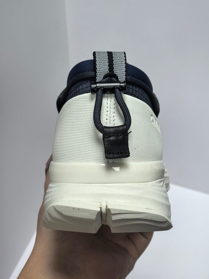 Scarpa sportiva moderna bianca con dettagli navy, tallone prominente e passante pratico.