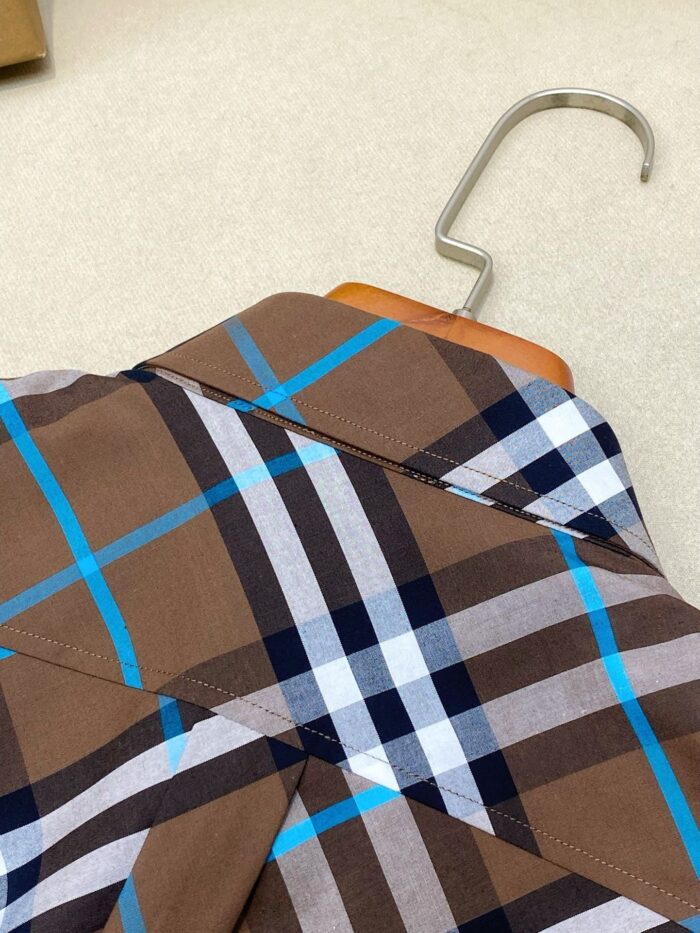 Camicia a quadri marrone e blu su appendiabiti in legno, stile casual e di qualità.