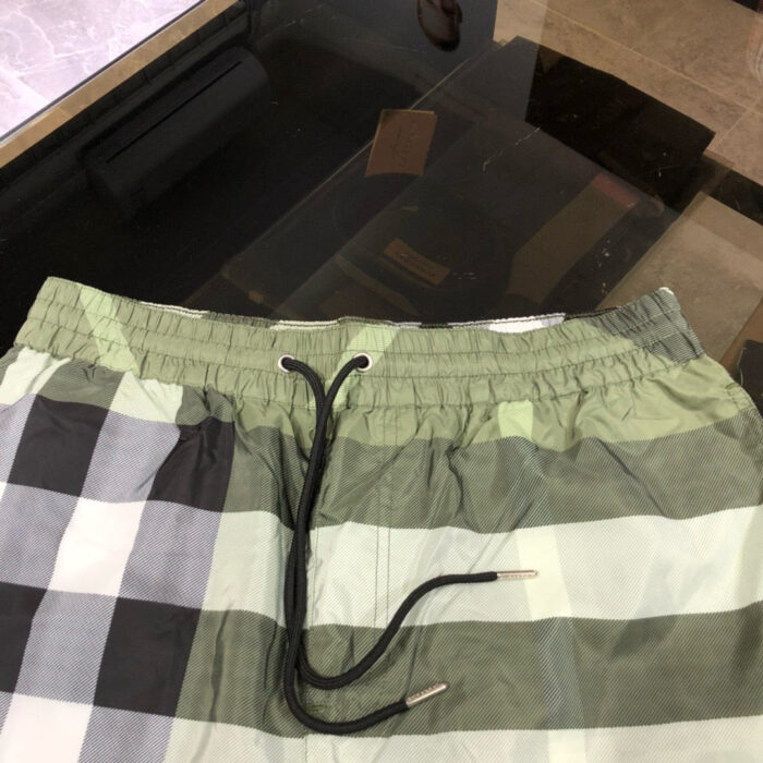 Pantaloncini da spiaggia checkered verde e grigio con cinturino elastico e aglet metallico.