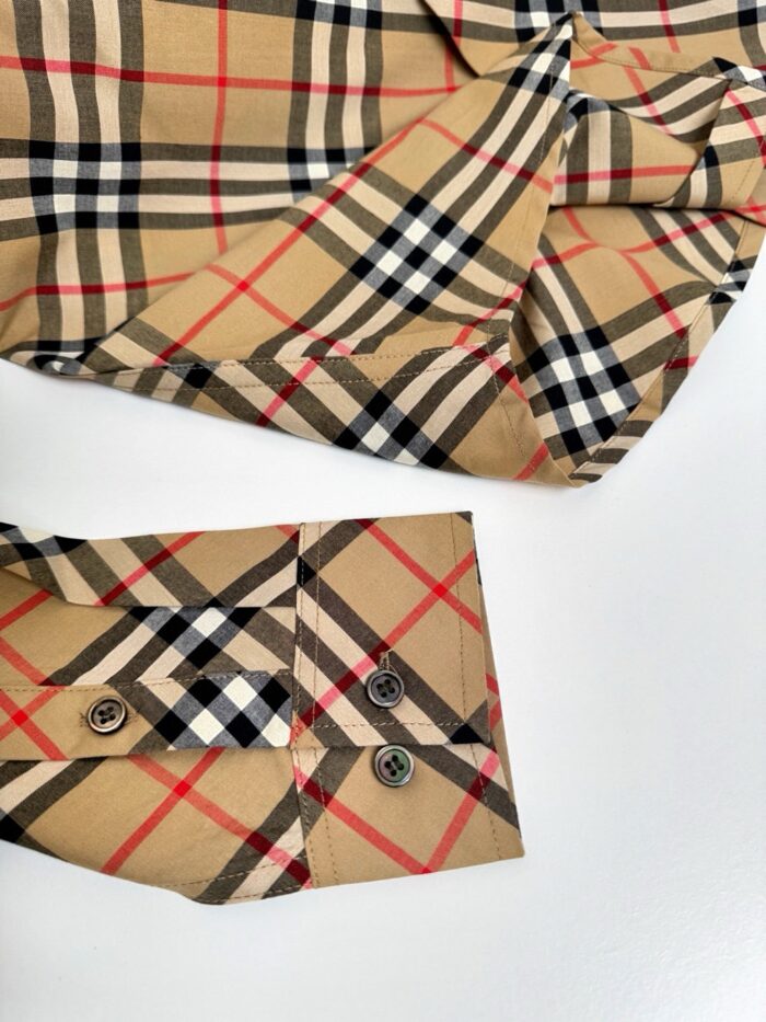 Dettaglio polsino camicia a quadri in tessuto di lusso con bottoni scuri.